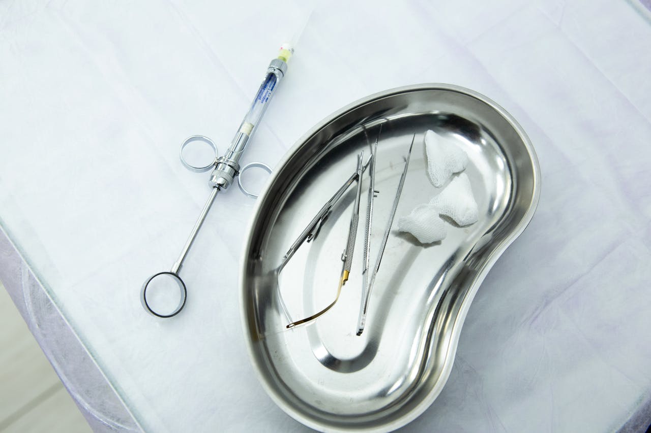 A set of sterile medical tools and syringe displayed in a kidney tray for dental or surgical use.